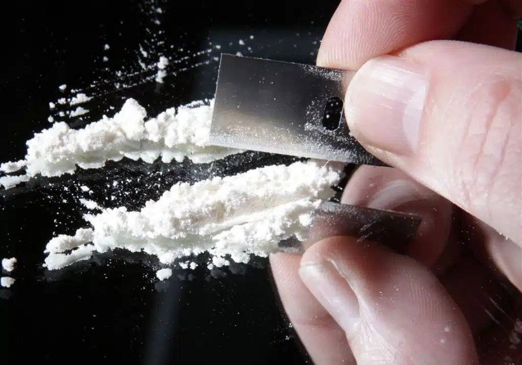 Cocaine and Methamphetamine Addiction abuse represented by crystal meth and powdered cocaine on a dark surface.