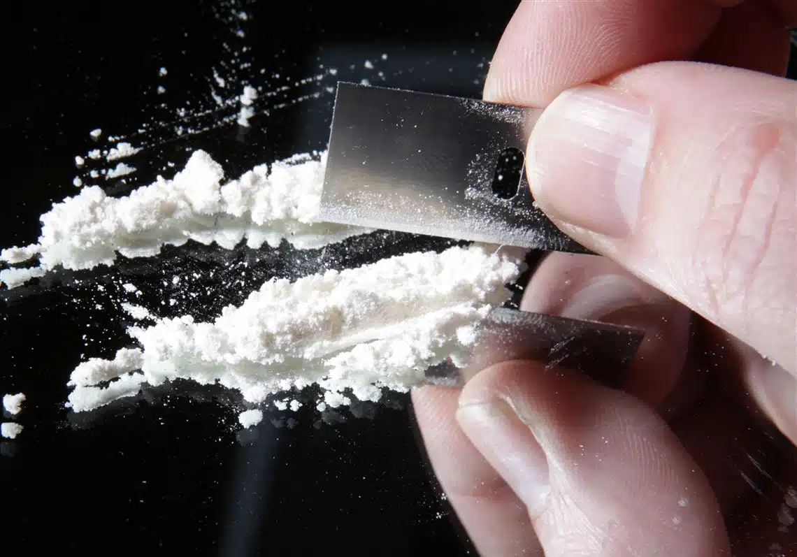Cocaine and Methamphetamine Addiction abuse represented by crystal meth and powdered cocaine on a dark surface.