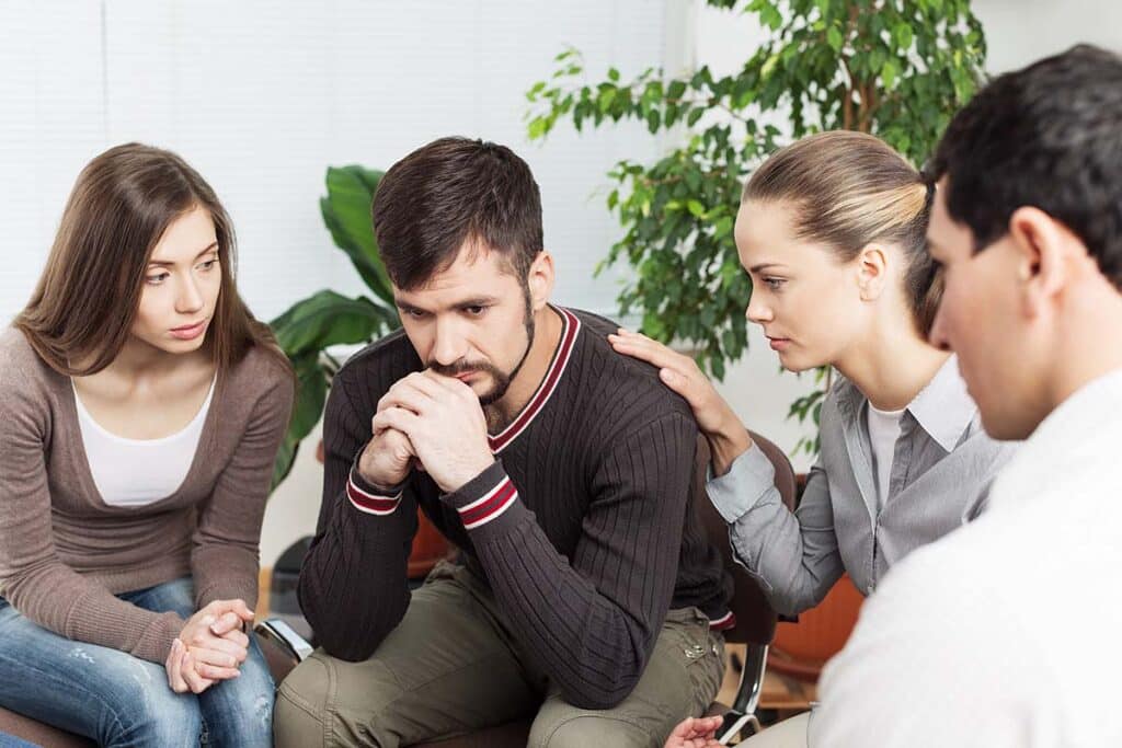 A diverse group of people, including family members and a professional, sit around a table, some writing on notepads, others listening intently. The atmosphere is serious but supportive, suggesting a planning meeting for an important family discussion. - Family drug intervention A diverse group of people, including family members and a professional, sit around a table, some writing on notepads, others listening intently. The atmosphere is serious but supportive, suggesting a planning meeting for an important family discussion. - Family drug intervention