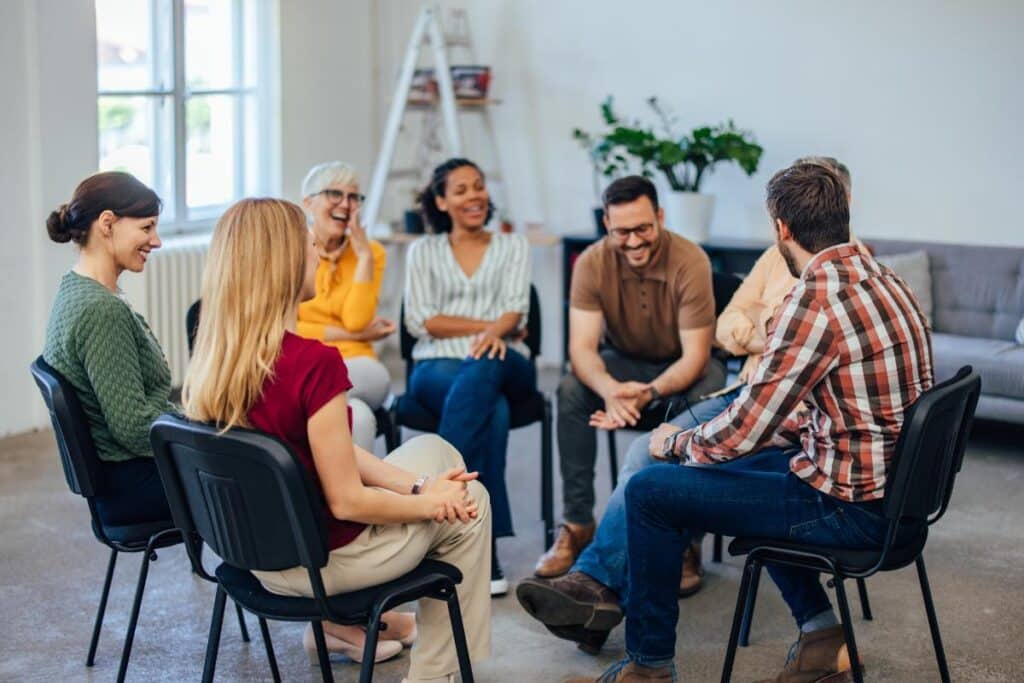 group of people sitting in a circle writing or reading letters - Mental health intervention