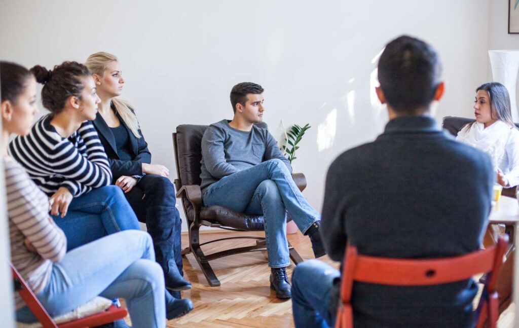 A group of people in a support group meeting, listening to a speaker and offering encouragement to one another. - detox for alcohol