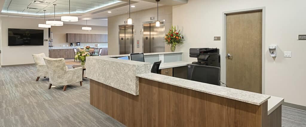A warm, welcoming rehab facility lobby with natural light, comfortable seating, and a friendly intake counselor speaking with a hopeful individual. Alt: free rehab centers near me welcoming environment.